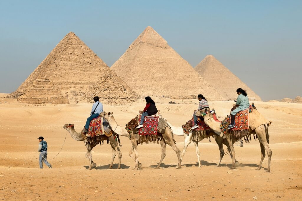 Tourists riding camels near the Great Pyramids of Giza, Egypt under clear skies.